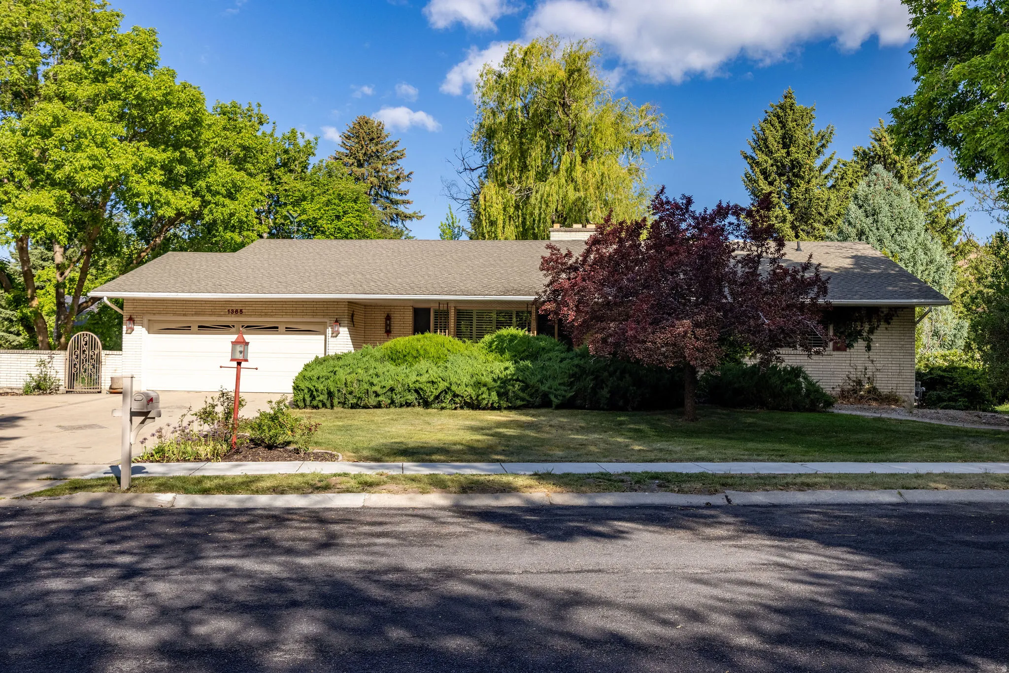 Ranch-style exterior with a two-car garage, mature landscaping, and a paved driveway