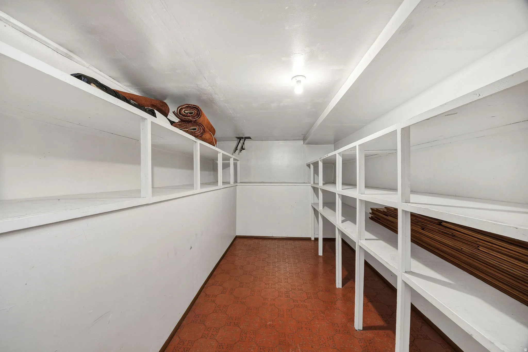 Dedicated storage room featuring extensive built-in shelving, durable floor tile, and overhead lighting