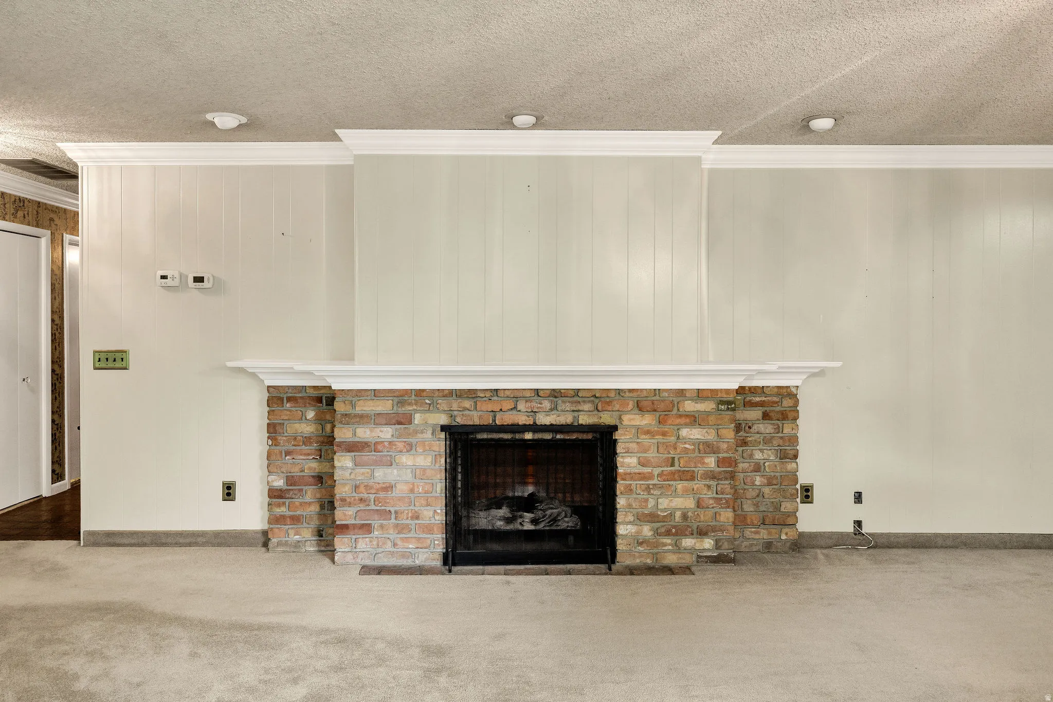 Brick fireplace with a black metal screen, a white mantel, and crown molding