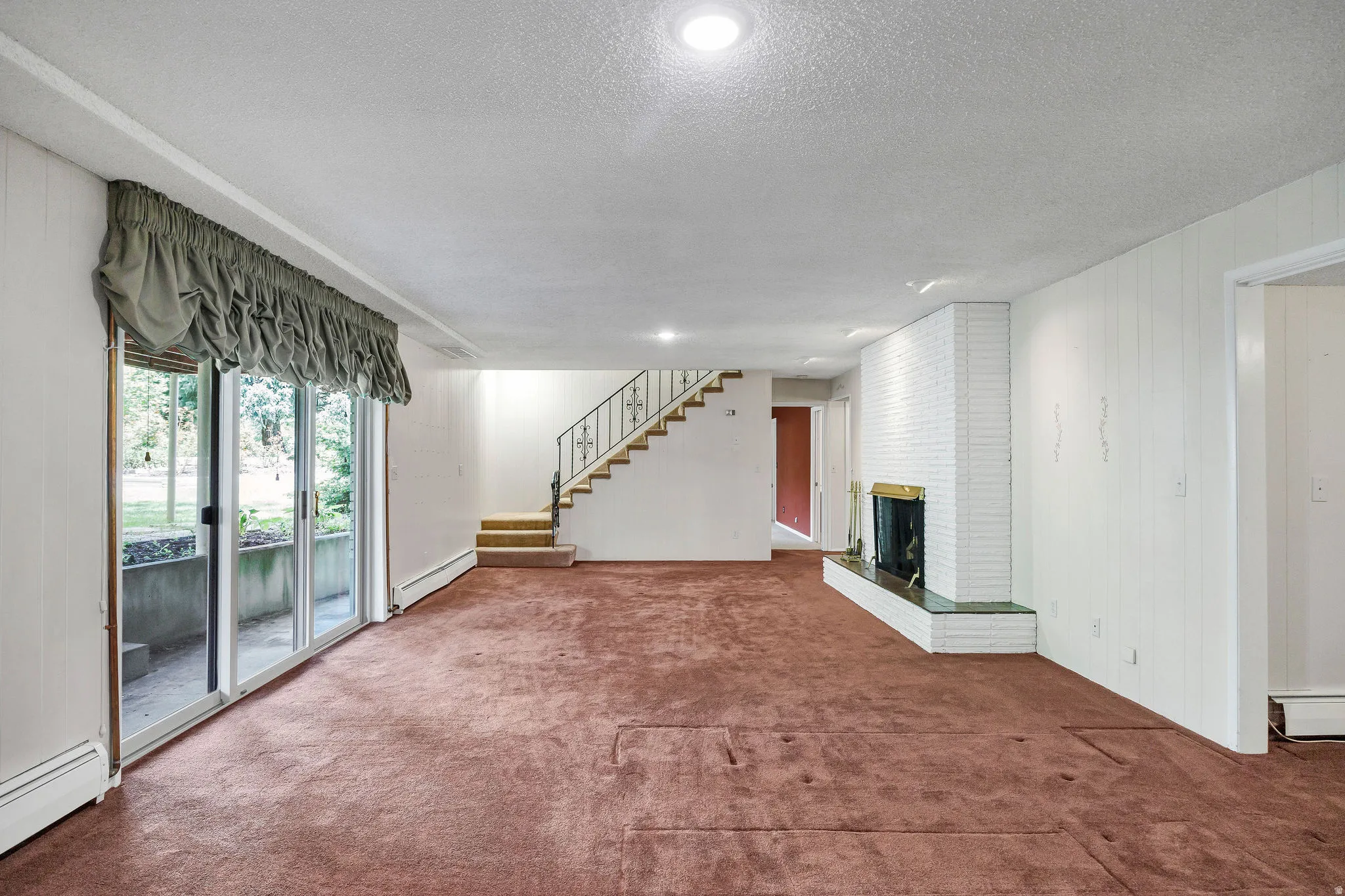 Spacious room featuring broadloom carpeting, a white brick fireplace with a brass-toned insert and green stone hearth, and white vertical paneling