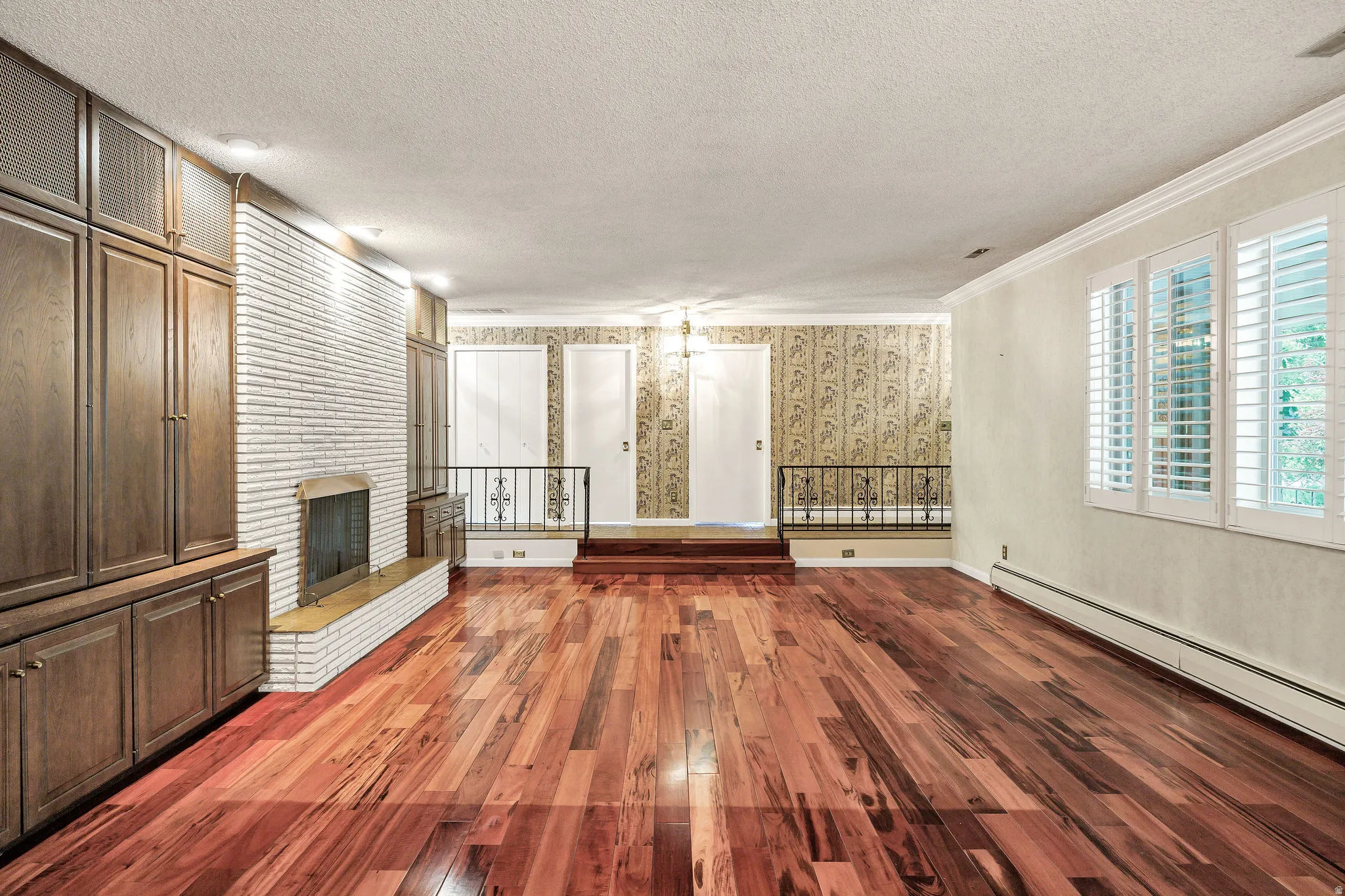 Expansive room featuring rich wood-finish flooring, a white brick fireplace with a hearth, and substantial built-in cabinetry
