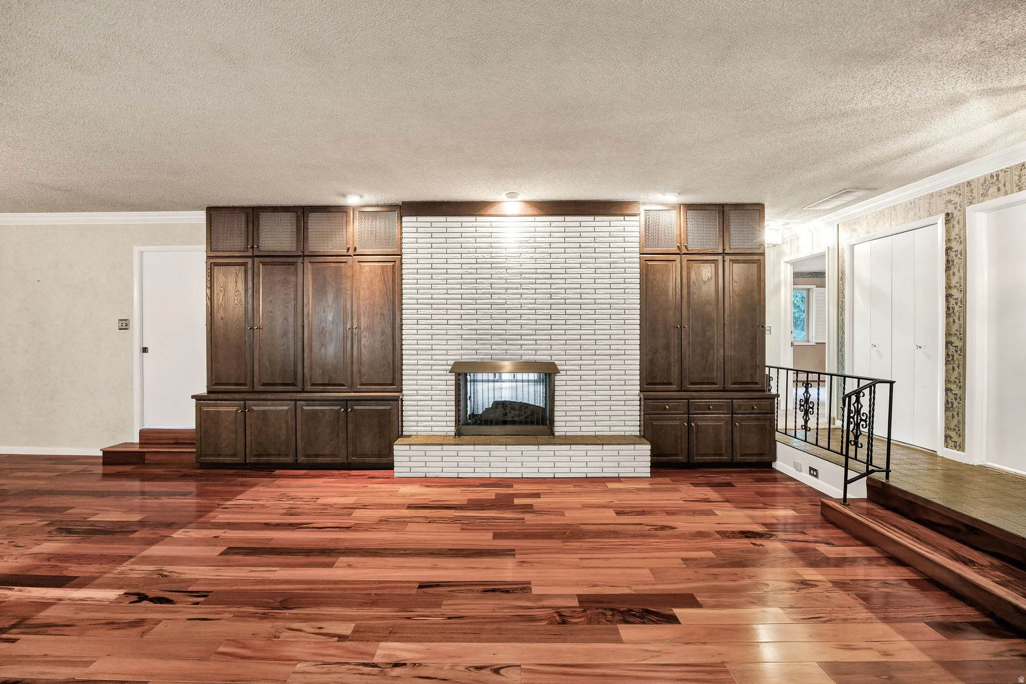 Spacious room featuring wood-finish flooring and a central fireplace with a white brick surround and hearth