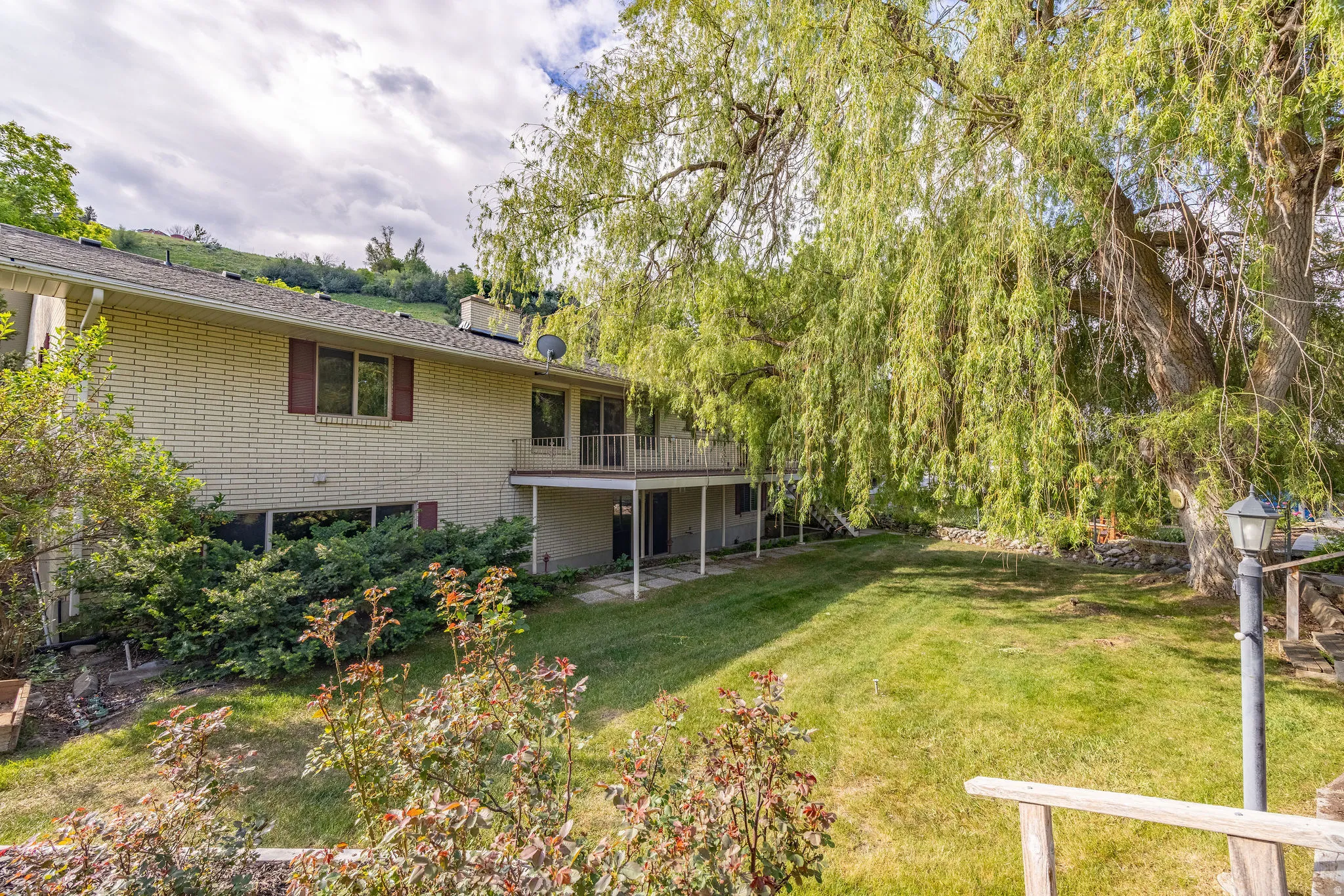 Rear exterior featuring a brick facade, upper-level balcony, and lower-level patio with stone pavers