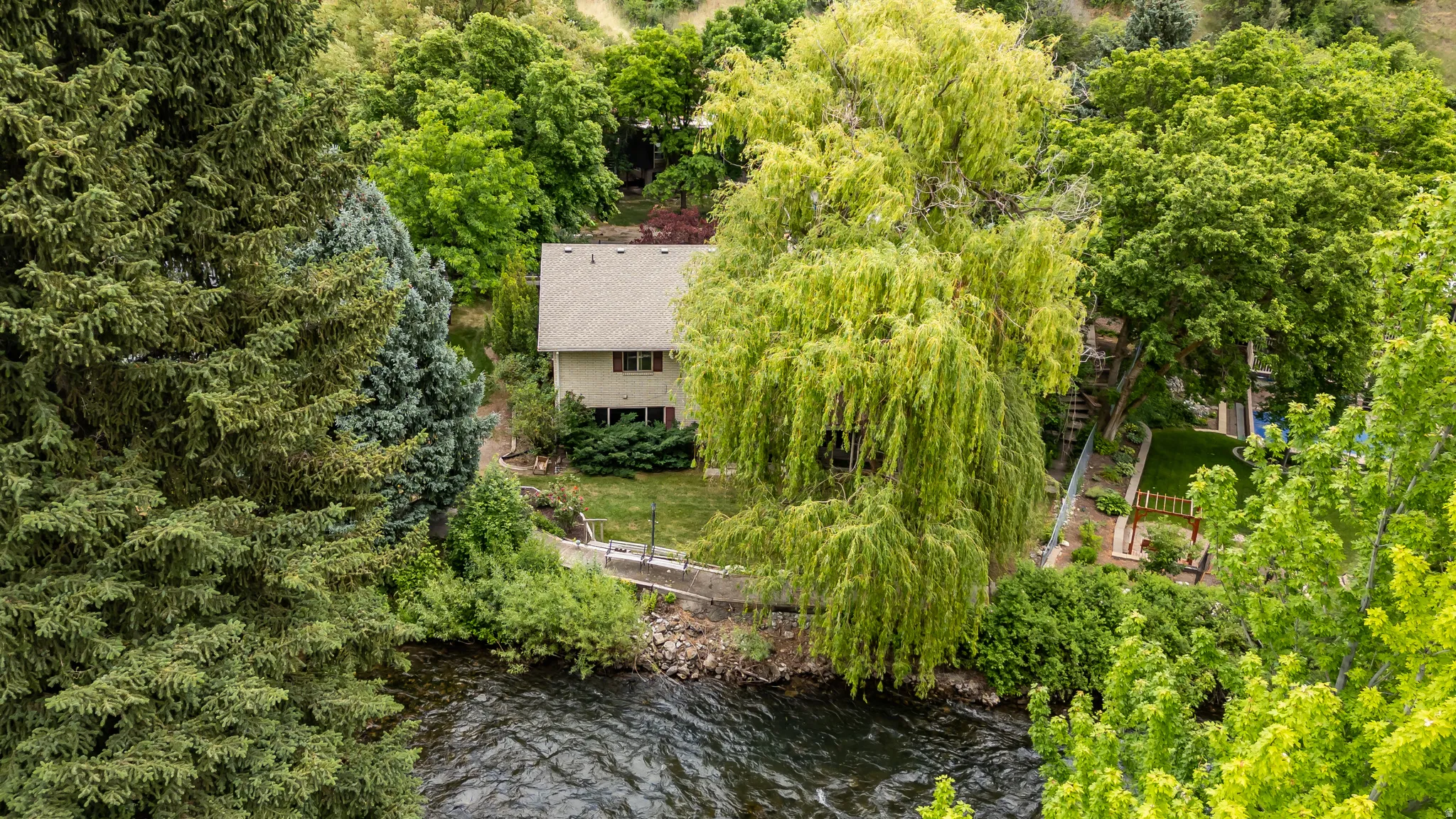Two-story residence with a light-toned exterior and a gabled roof, nestled among abundant mature trees