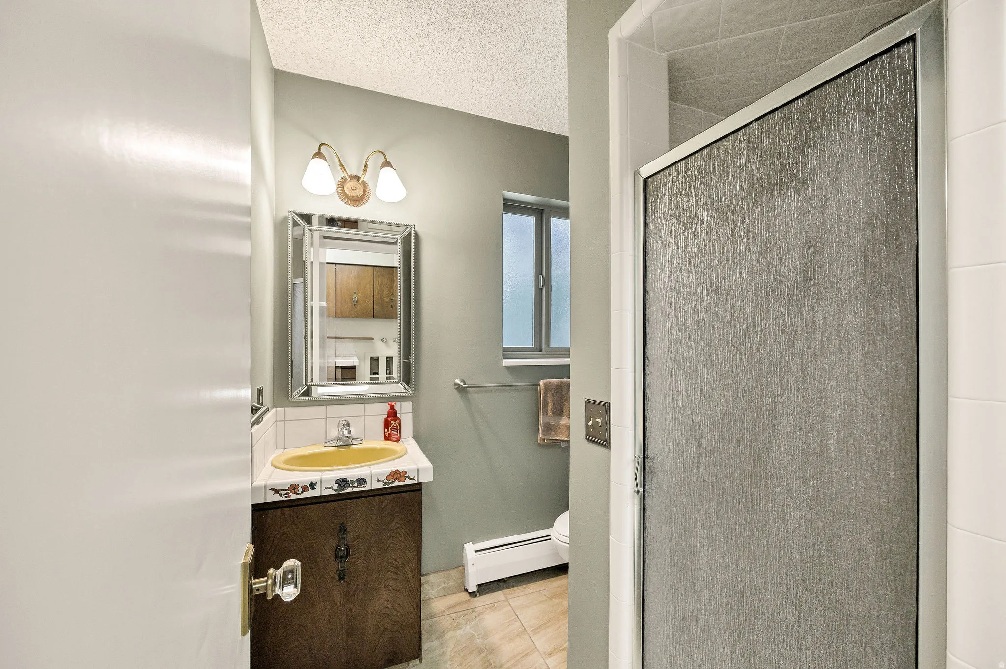 Bathroom featuring a decorative vanity mirror, a vanity light fixture with two sconces, a wood-finish vanity cabinet, and an enclosed shower with textured glass