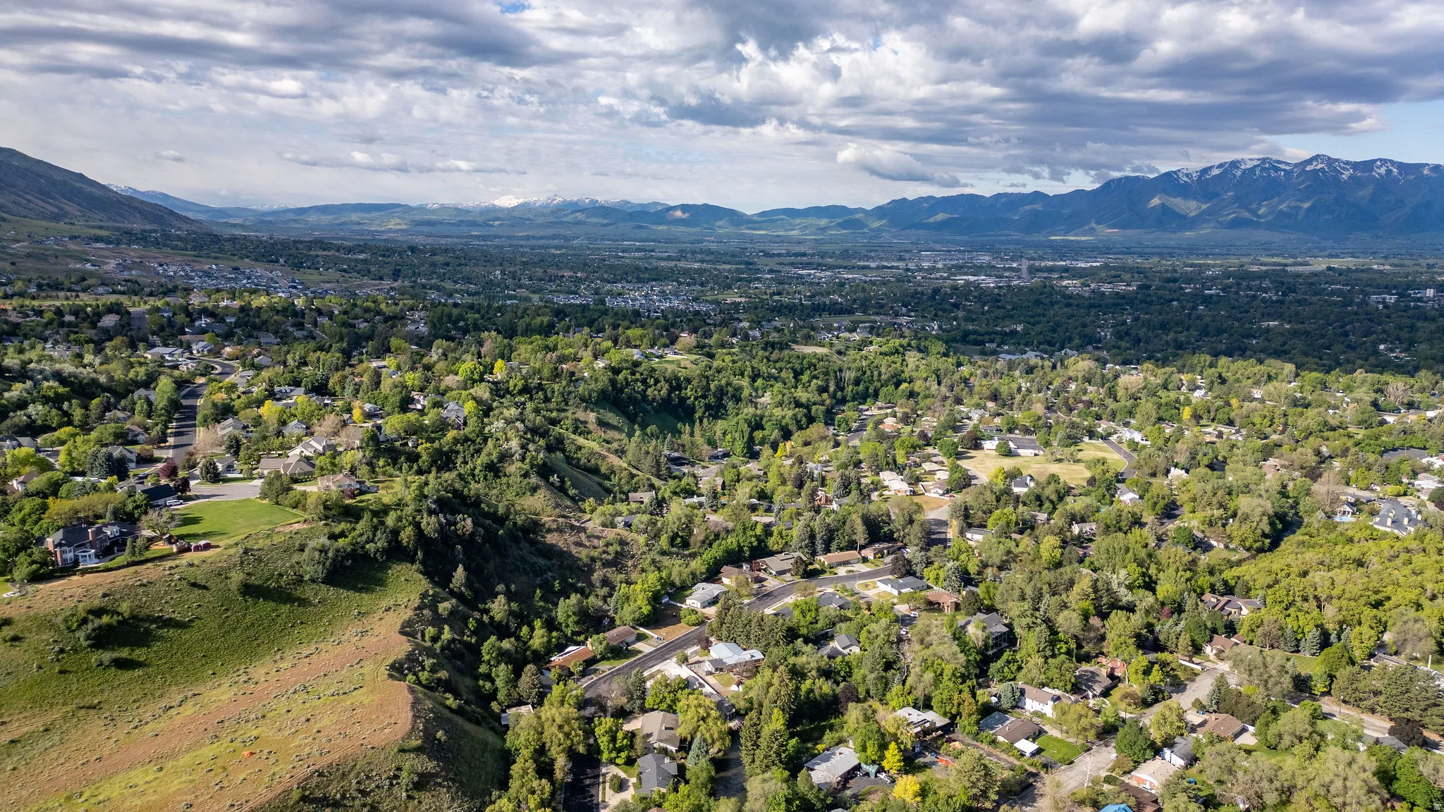 Expansive aerial perspective showcasing a developed residential area with abundant mature trees and mountainous terrain