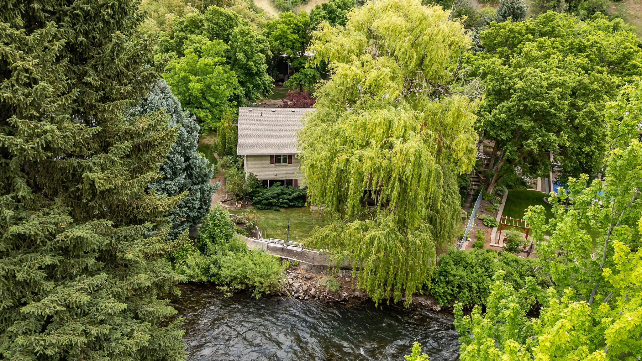 Riverside property featuring a two-story residence with a gabled roof and surrounding mature trees