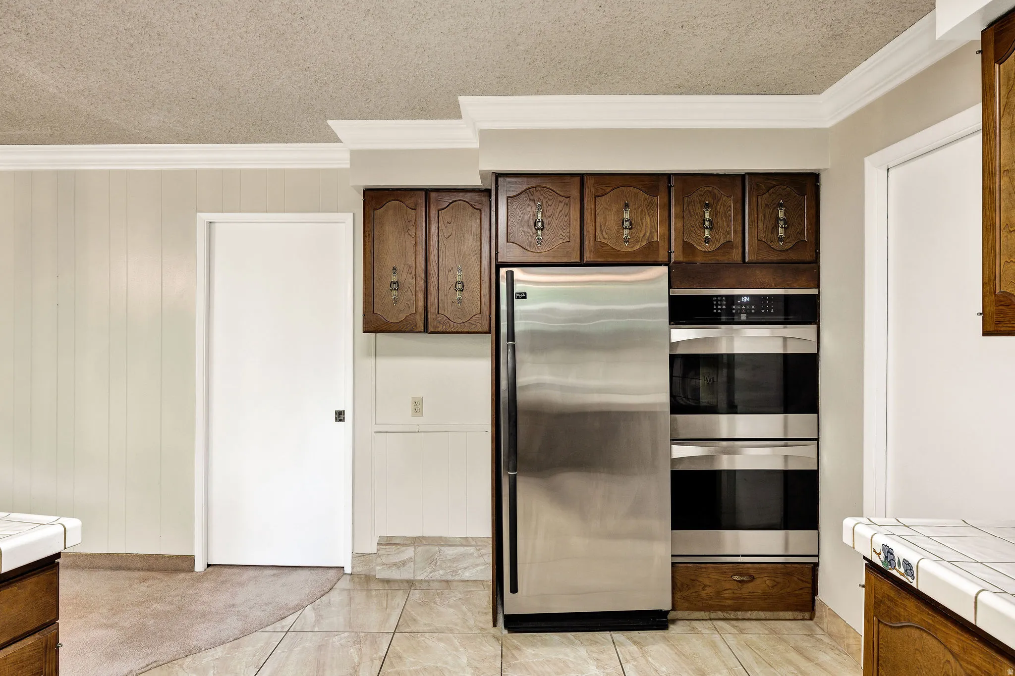 Kitchen area featuring stainless steel refrigerator, double wall ovens, wood cabinetry, and tile flooring
