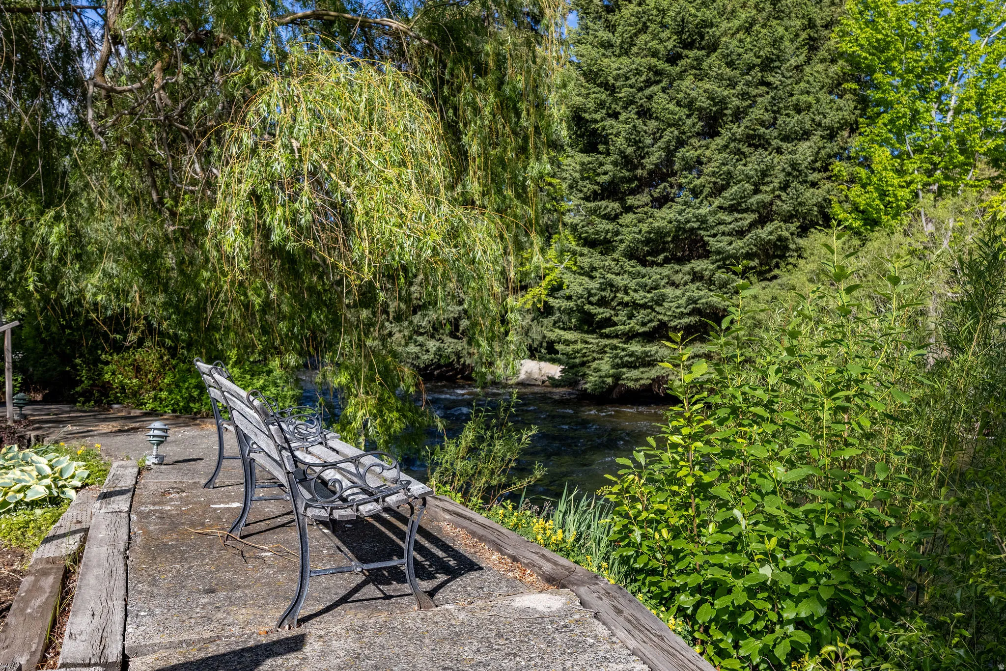Waterside patio featuring a concrete surface, wooden borders, and a decorative metal bench
