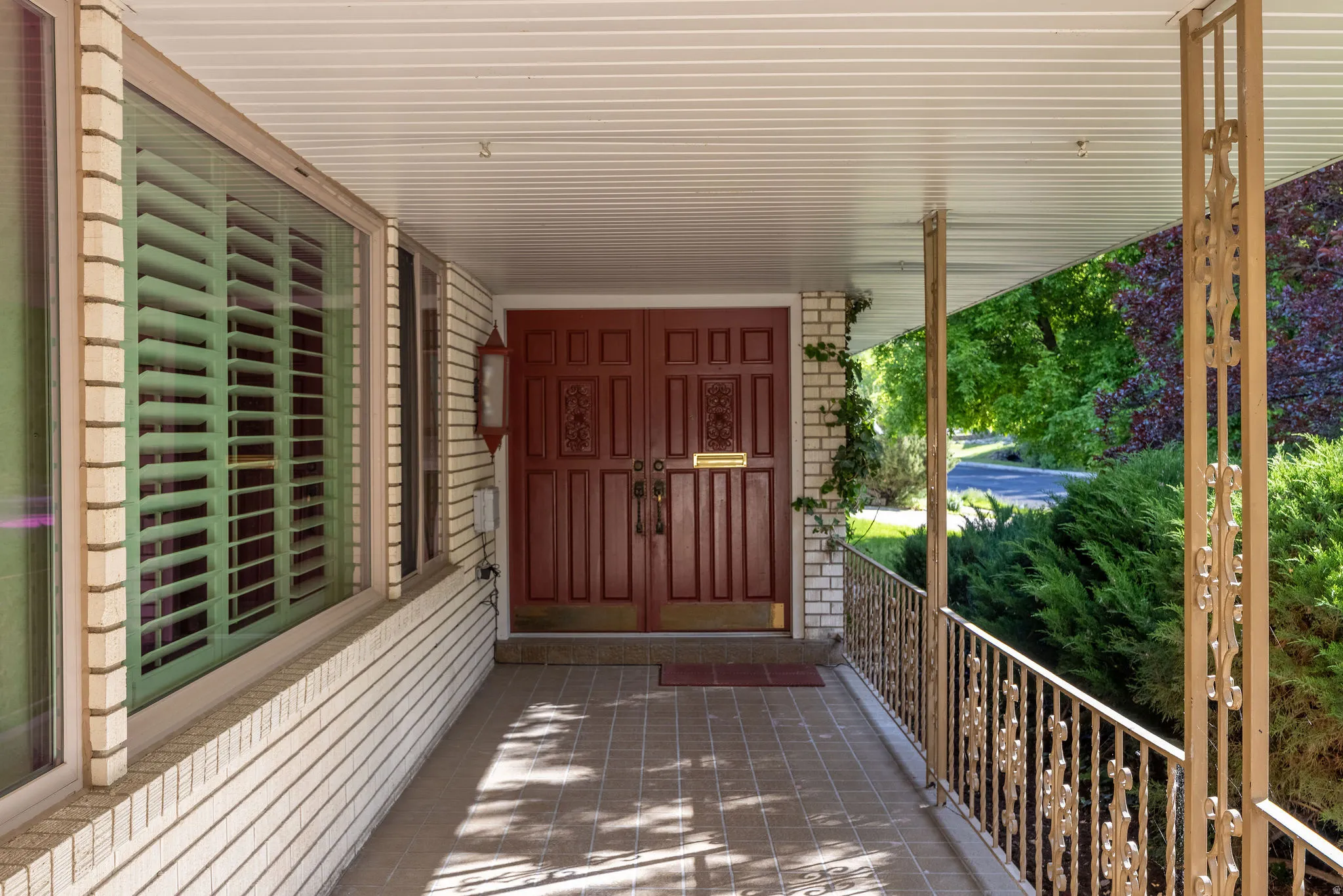 Covered front porch featuring a brick facade, decorative iron railings, and a tiled floor