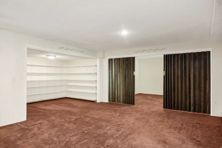 Spacious room with plush carpeting, featuring built-in shelving, a recessed ceiling light, and bi-fold wood-finish doors