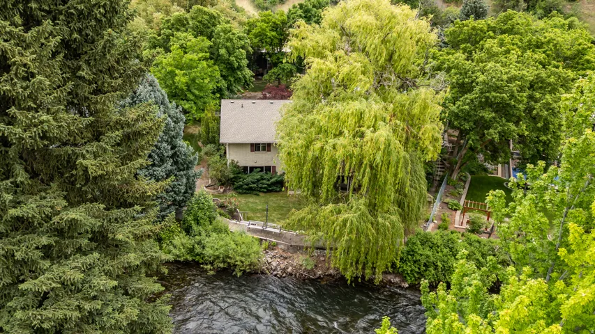 Two-story residence with a light-toned exterior and a gabled roof, nestled among abundant mature trees