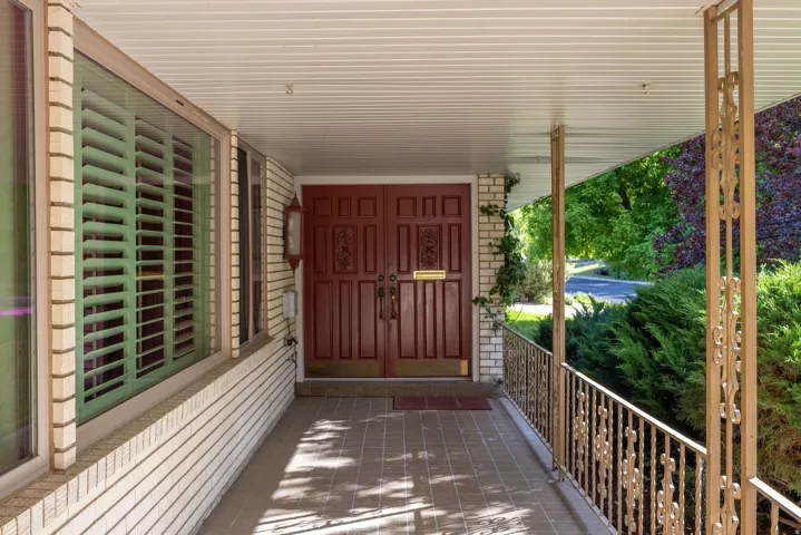 Covered front porch featuring a brick facade, decorative iron railings, and a tiled floor