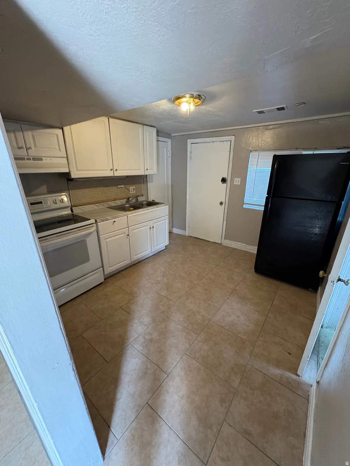 Kitchen featuring light-toned tile flooring, white cabinetry, a white electric range with a built-in microwave, and a black refrigerator
