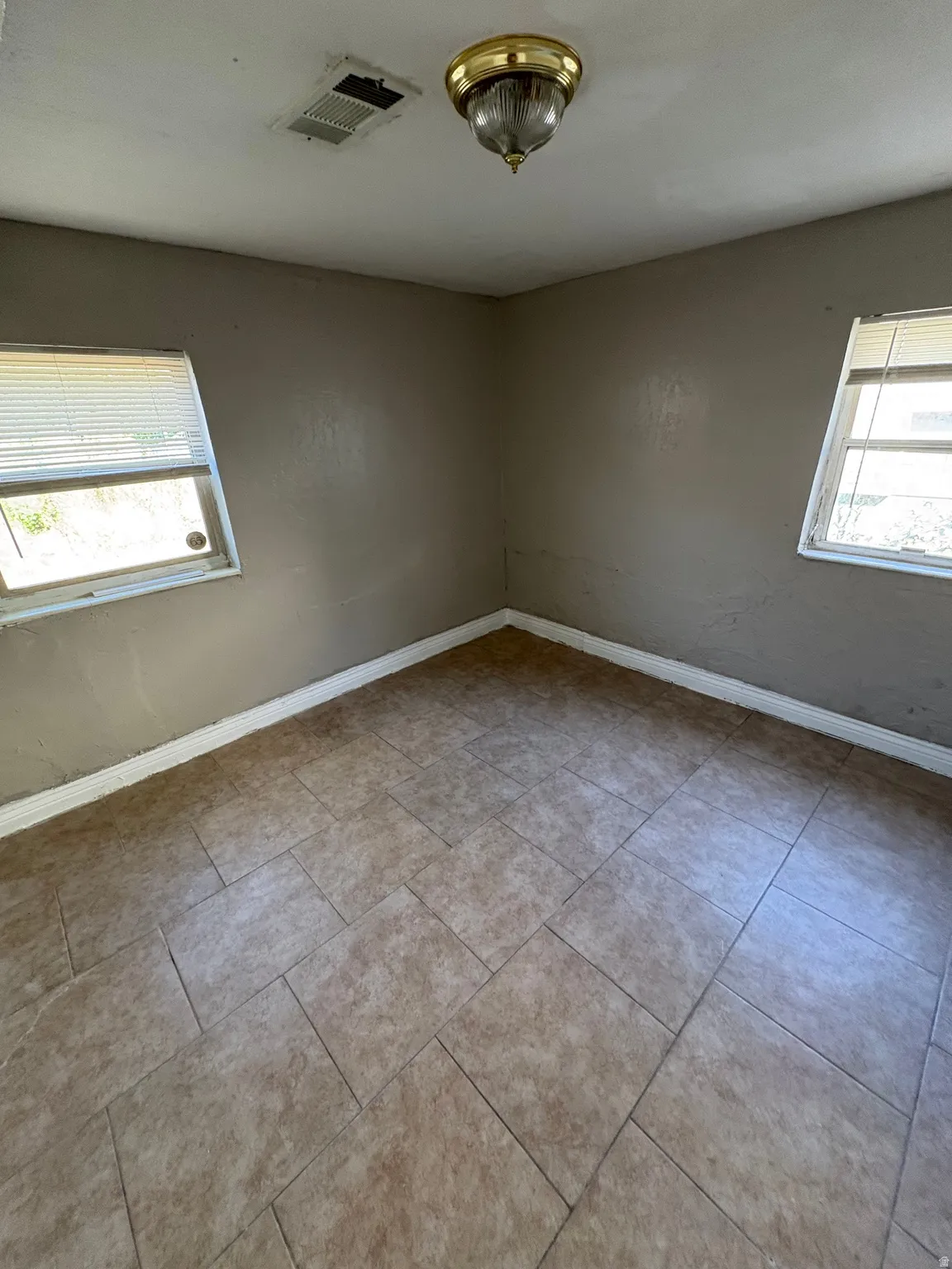 Room featuring tiled flooring, a ceiling-mounted light fixture, and two windows with horizontal blinds