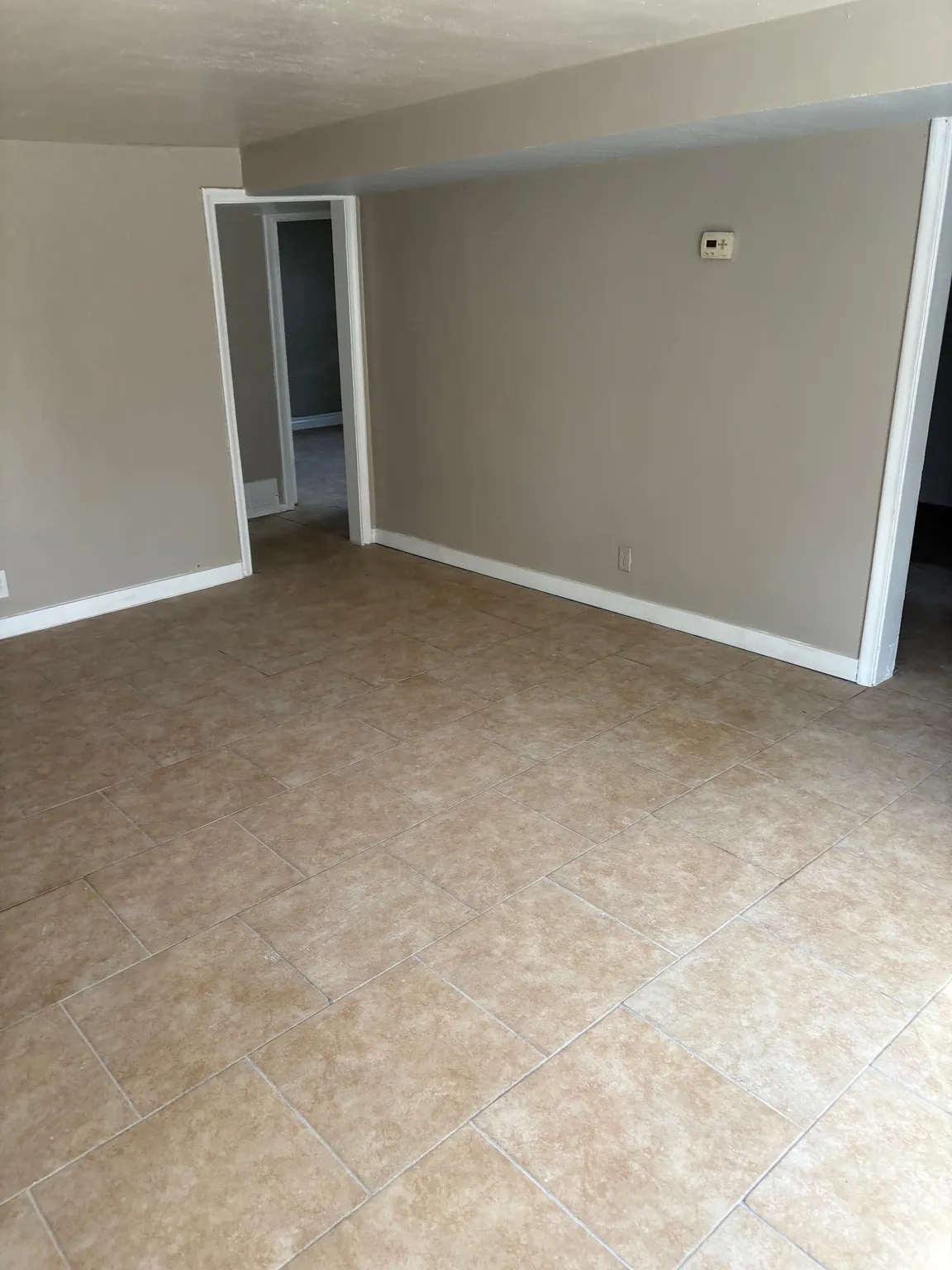 Spacious interior room featuring light-colored tile flooring, neutral wall paint, and white trim