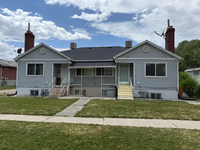 Duplex property featuring gray siding, a dark asphalt shingle roof, and two prominent brick chimneys