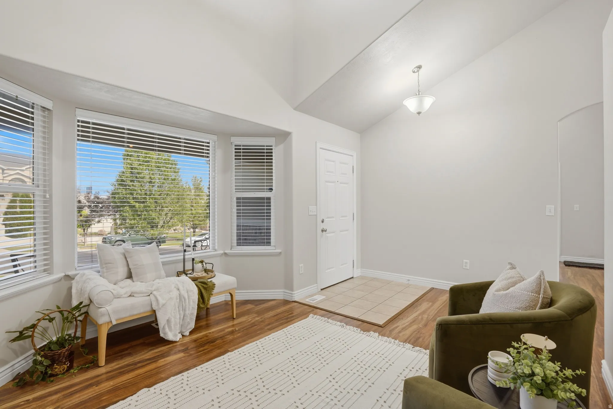 Spacious living area featuring a bay window, vaulted ceilings, wood-finish flooring, a tiled entry, and a paneled front door