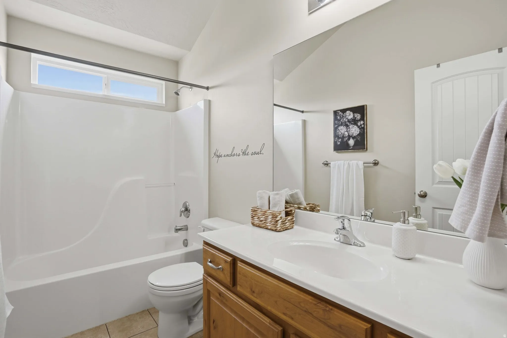 Bathroom featuring a white integrated tub/shower unit with chrome fixtures, a wood-finish vanity with a white countertop and integrated sink, a large wall-mounted mirror, and tile flooring