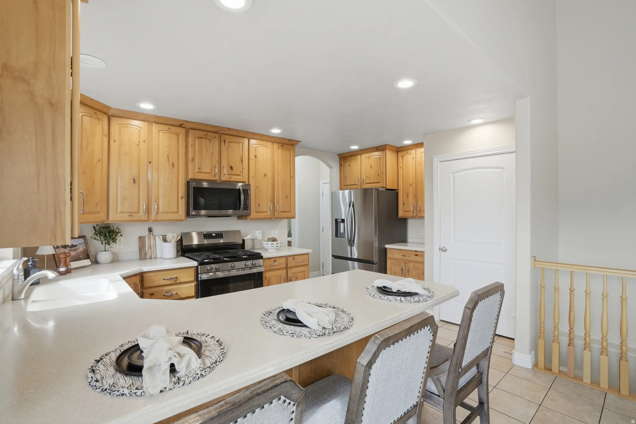 Kitchen featuring light wood cabinetry, white countertops, stainless steel appliances, recessed ceiling lighting, and a breakfast bar with seating