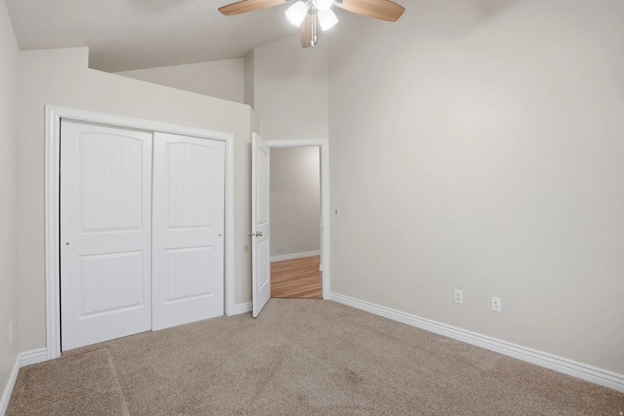 Spacious bedroom featuring vaulted ceilings, a large window, neutral carpeting, white baseboards, and a ceiling fan with light fixture