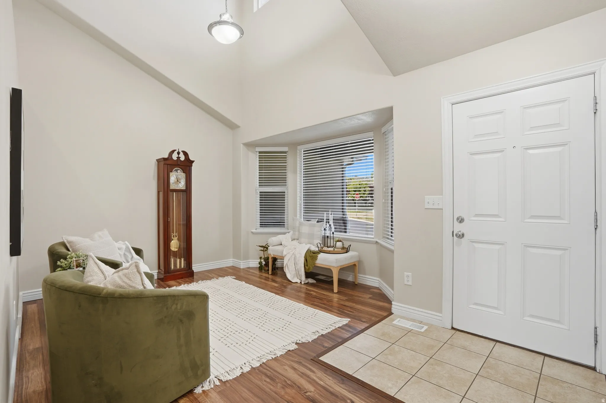Entryway featuring a paneled door, vaulted ceiling, bay window with blinds, wood-finish flooring, and tile flooring