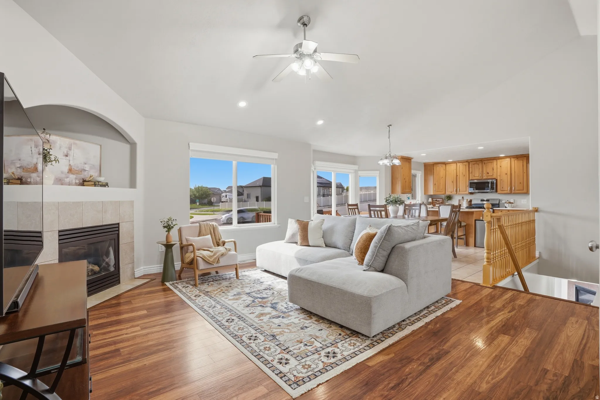 Spacious living area featuring wood-finish flooring, a tiled corner fireplace, and a ceiling fan
