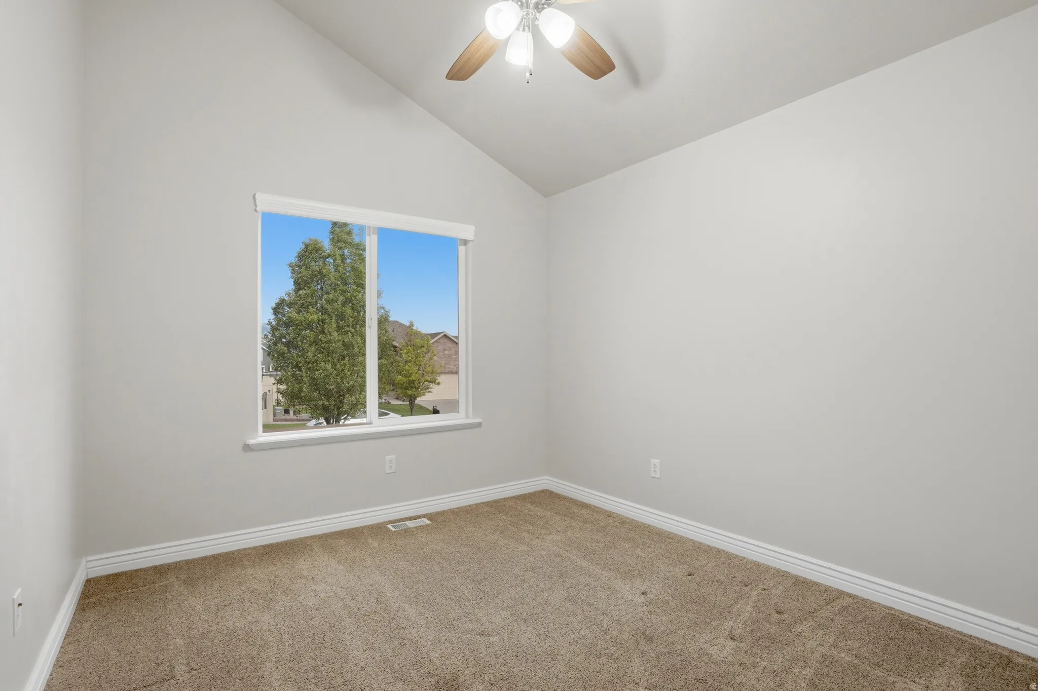 Spacious bedroom featuring vaulted ceilings, a large window, neutral carpeting, white baseboards, and a ceiling fan with light fixture
