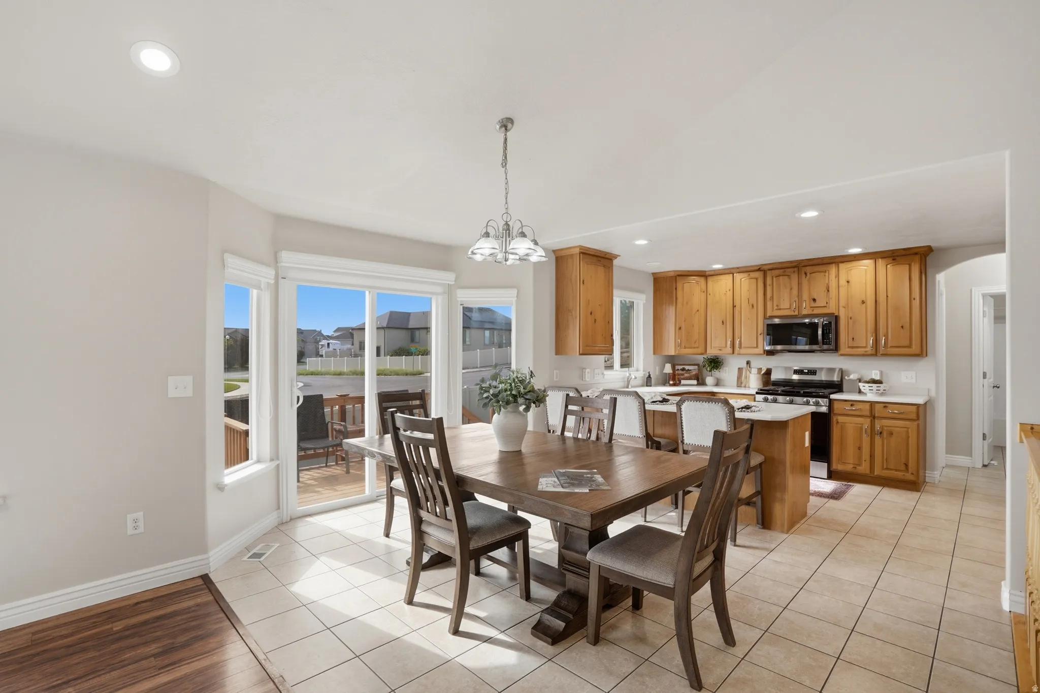 Open-concept kitchen and dining area featuring warm wood cabinetry, stainless steel appliances, and light-toned tile flooring