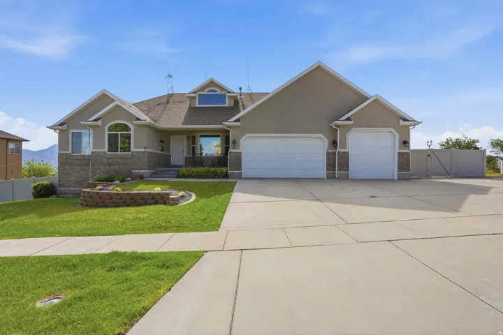Stucco and brick facade with a two-car garage, concrete driveway, and front lawn with a decorative retaining wall