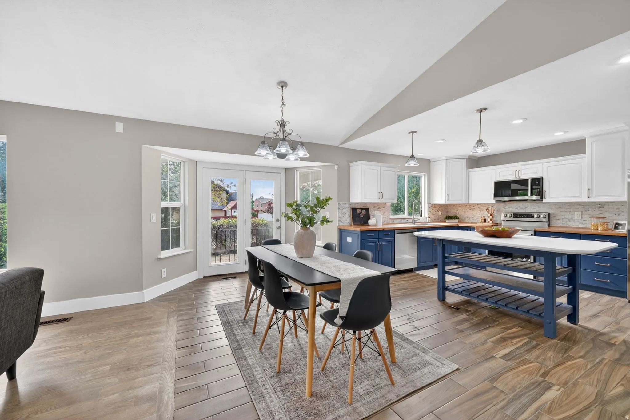 Spacious open-concept kitchen and dining area featuring dual-tone cabinetry, wood-finish countertops, stainless steel appliances, and a central island with integrated shelving