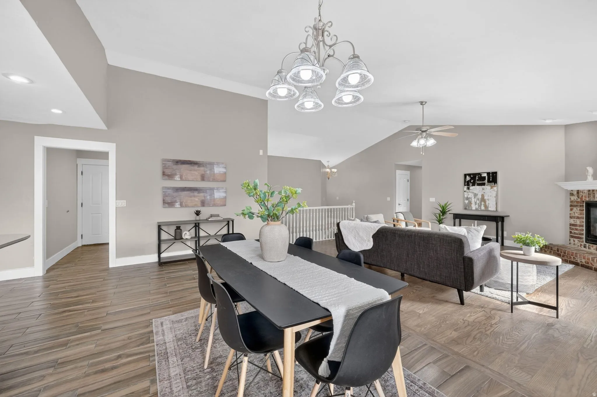 Open-concept living area featuring wood-finish flooring, vaulted ceilings, recessed lighting, and a brick fireplace