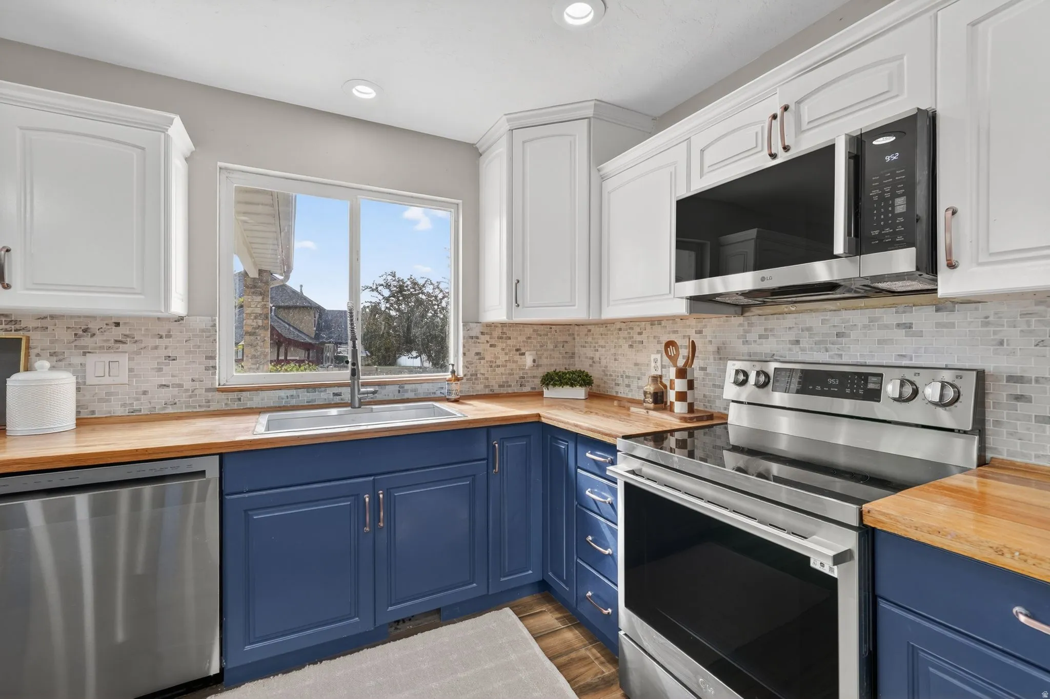 Modern kitchen featuring two-tone cabinetry, wood-finish countertops, stainless steel appliances, a mosaic tile backsplash, and an undermount sink