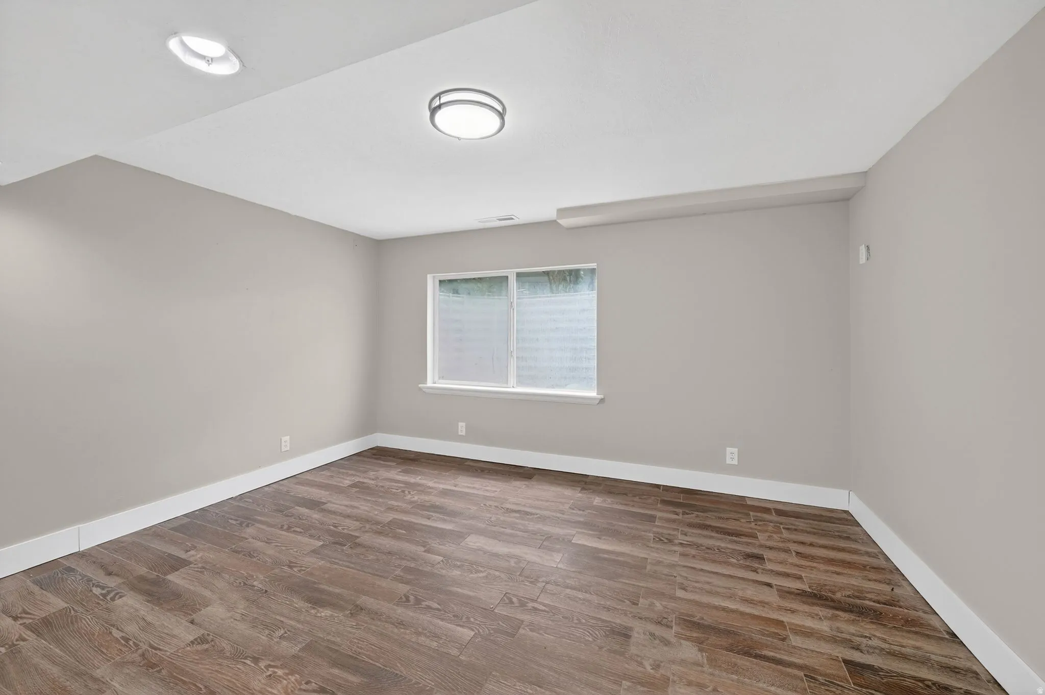 Spacious room featuring wood-finish flooring, light neutral walls, and crisp white baseboards