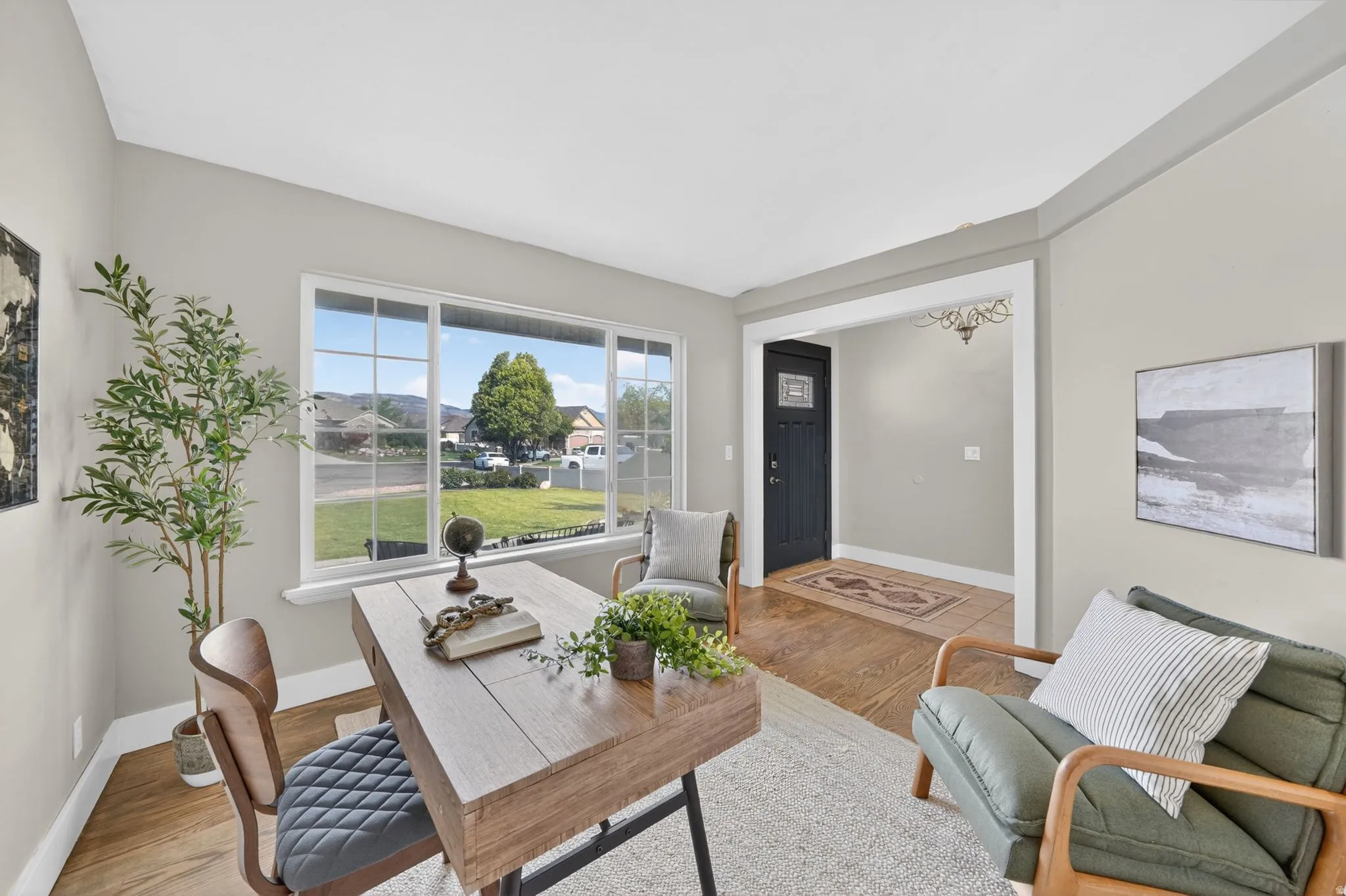 Bright living space featuring a large picture window with multiple panes, light-toned wall paint, wood-finish flooring, and a wide entryway