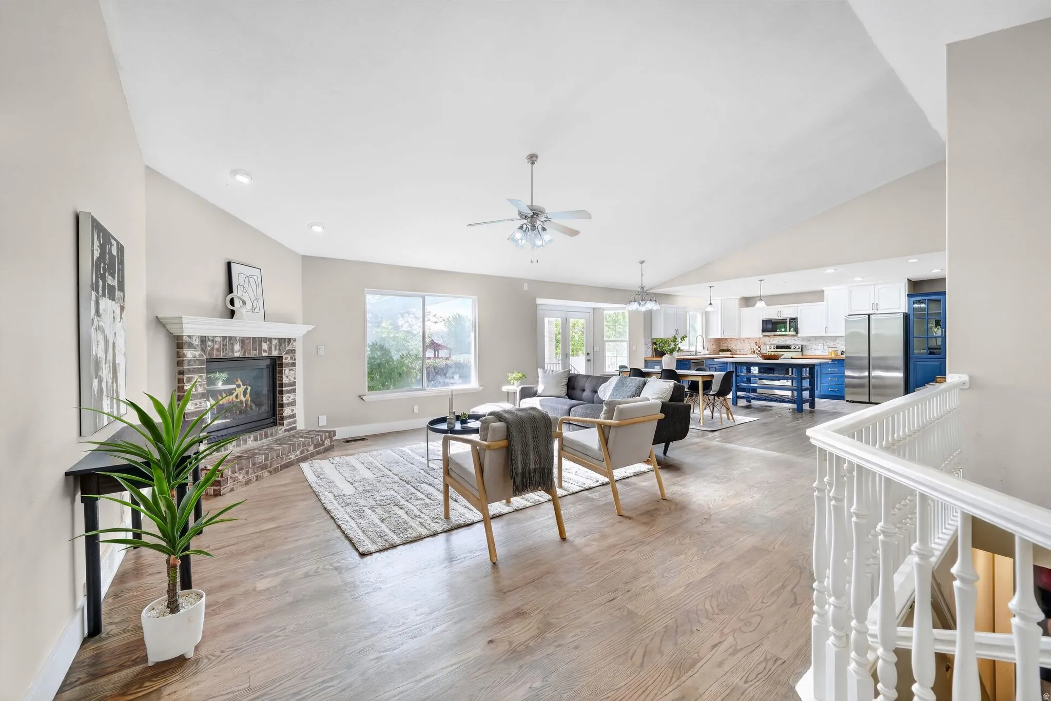 Spacious open-concept interior featuring wood-finish flooring, a brick fireplace with white mantel, and vaulted ceilings with recessed lighting