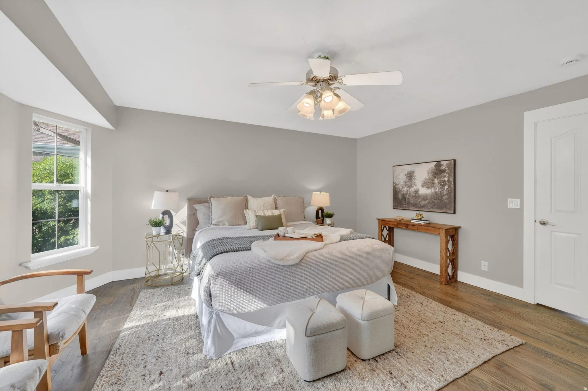 Spacious room featuring wood-finish flooring, a ceiling fan with integrated lighting, a single window, and a paneled door