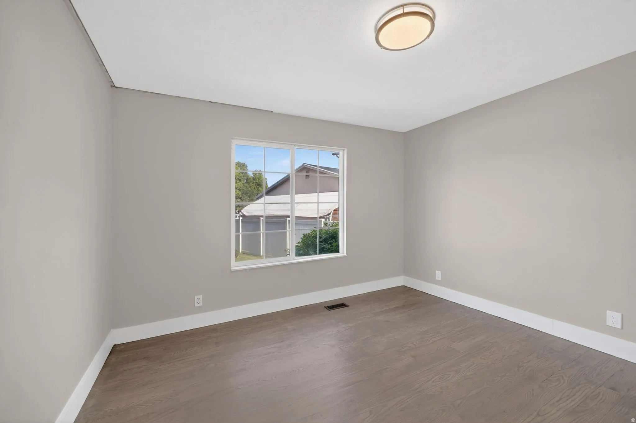 Neutral-toned interior room featuring wood-finish flooring, white baseboards, and a window with white trim