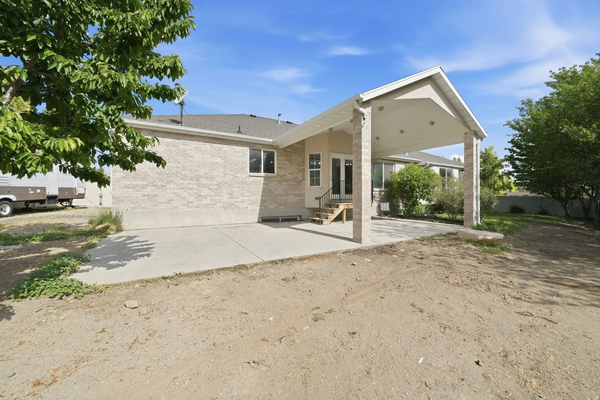 Rear exterior featuring a covered patio with recessed lighting, concrete patio, light-colored brick facade, and a multi-level wood deck with stairs