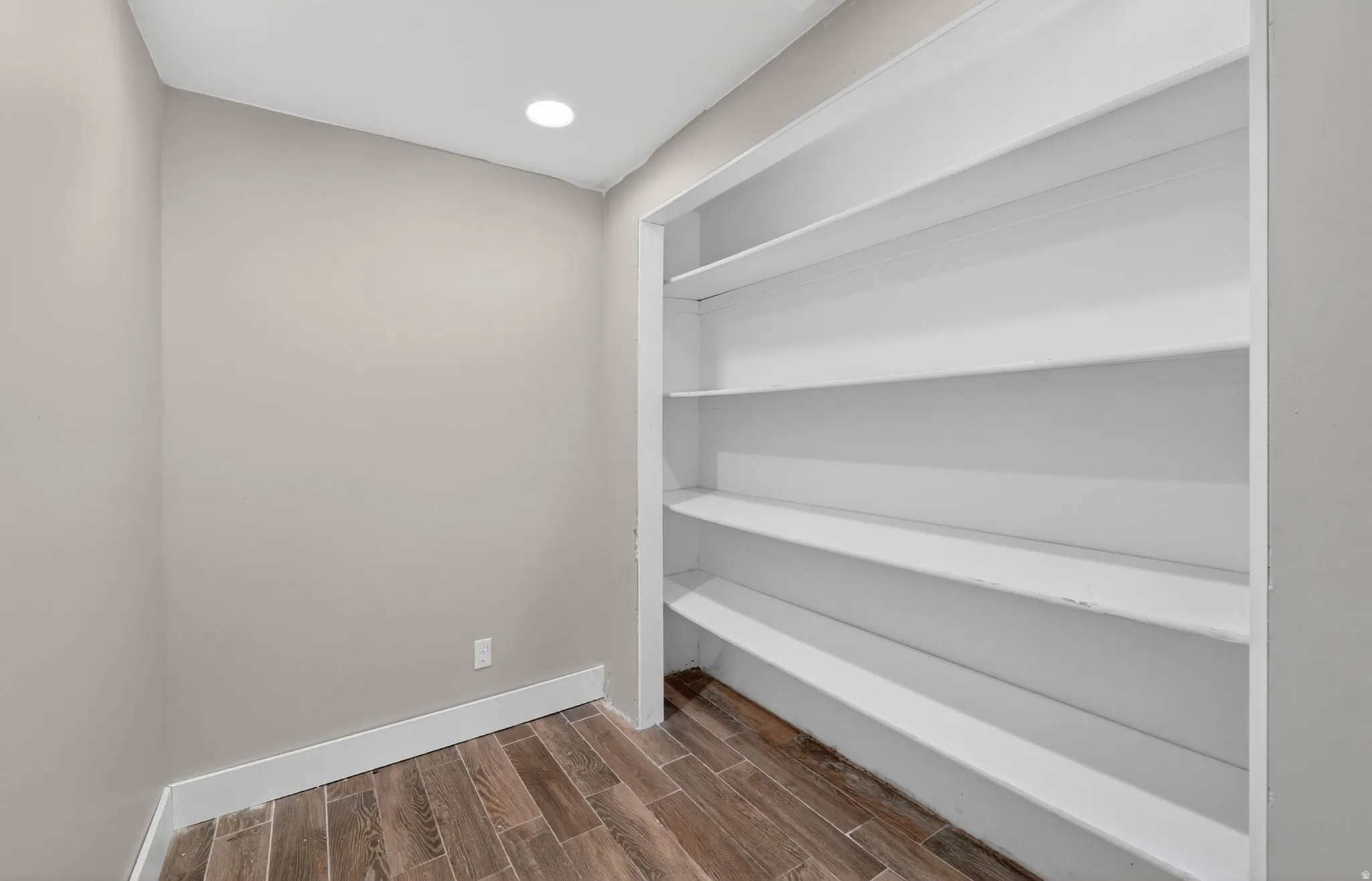 Built-in white shelving, wood-finish flooring, recessed lighting, neutral wall tones, and white baseboards
