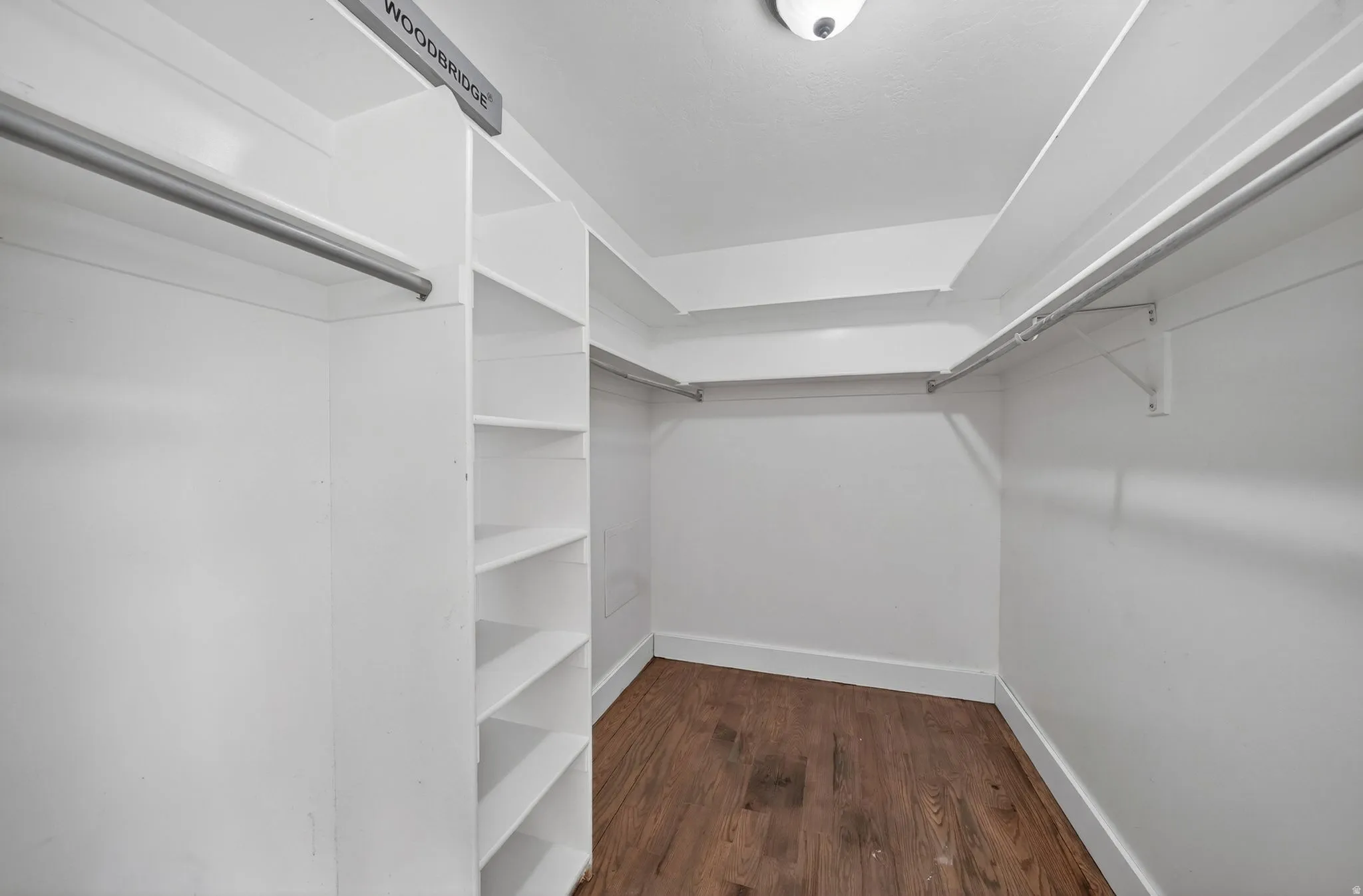 Walk-in closet featuring wood-finish flooring, white built-in shelving, white walls, and multiple clothing rods
