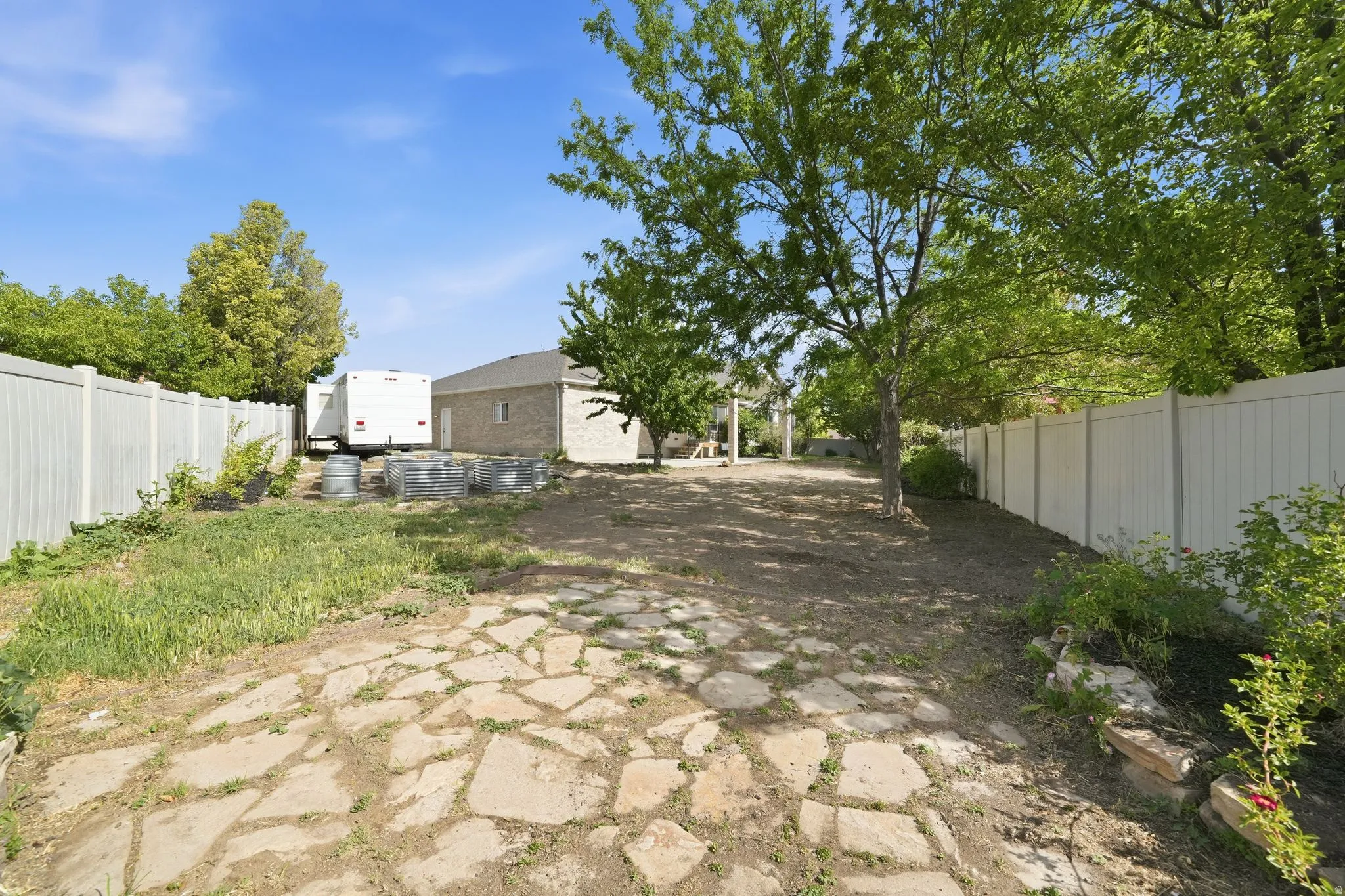 Spacious rear yard featuring a flagstone patio, mature trees, and perimeter fencing