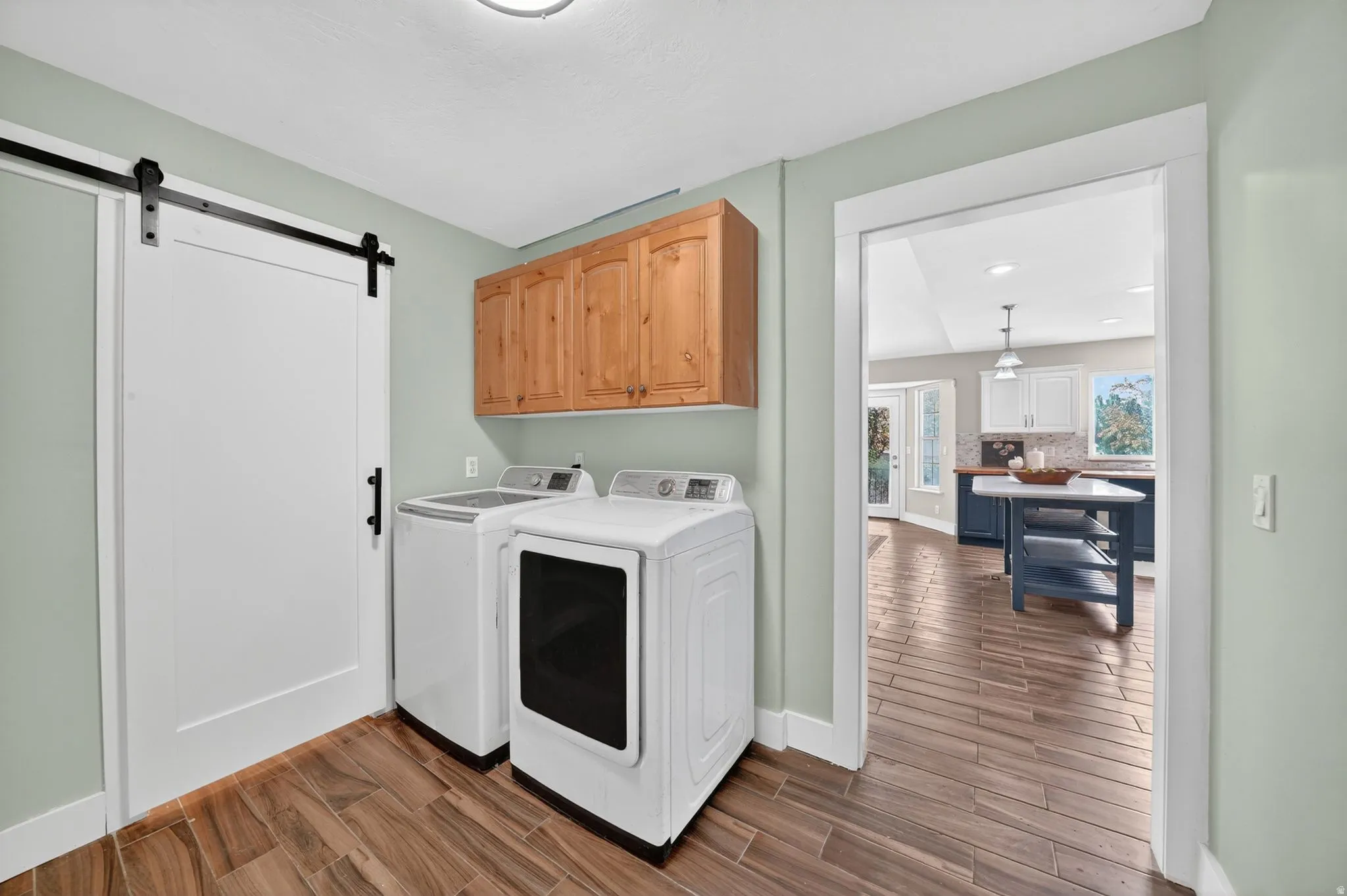 Dedicated laundry space featuring wood-finish flooring, a white barn door, and overhead wood cabinetry