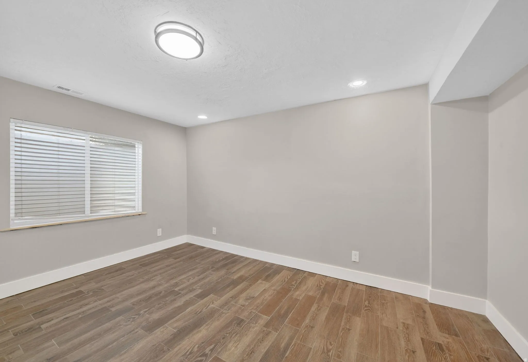Spacious room featuring wood-finish tile flooring, neutral wall tones, and bright white baseboards