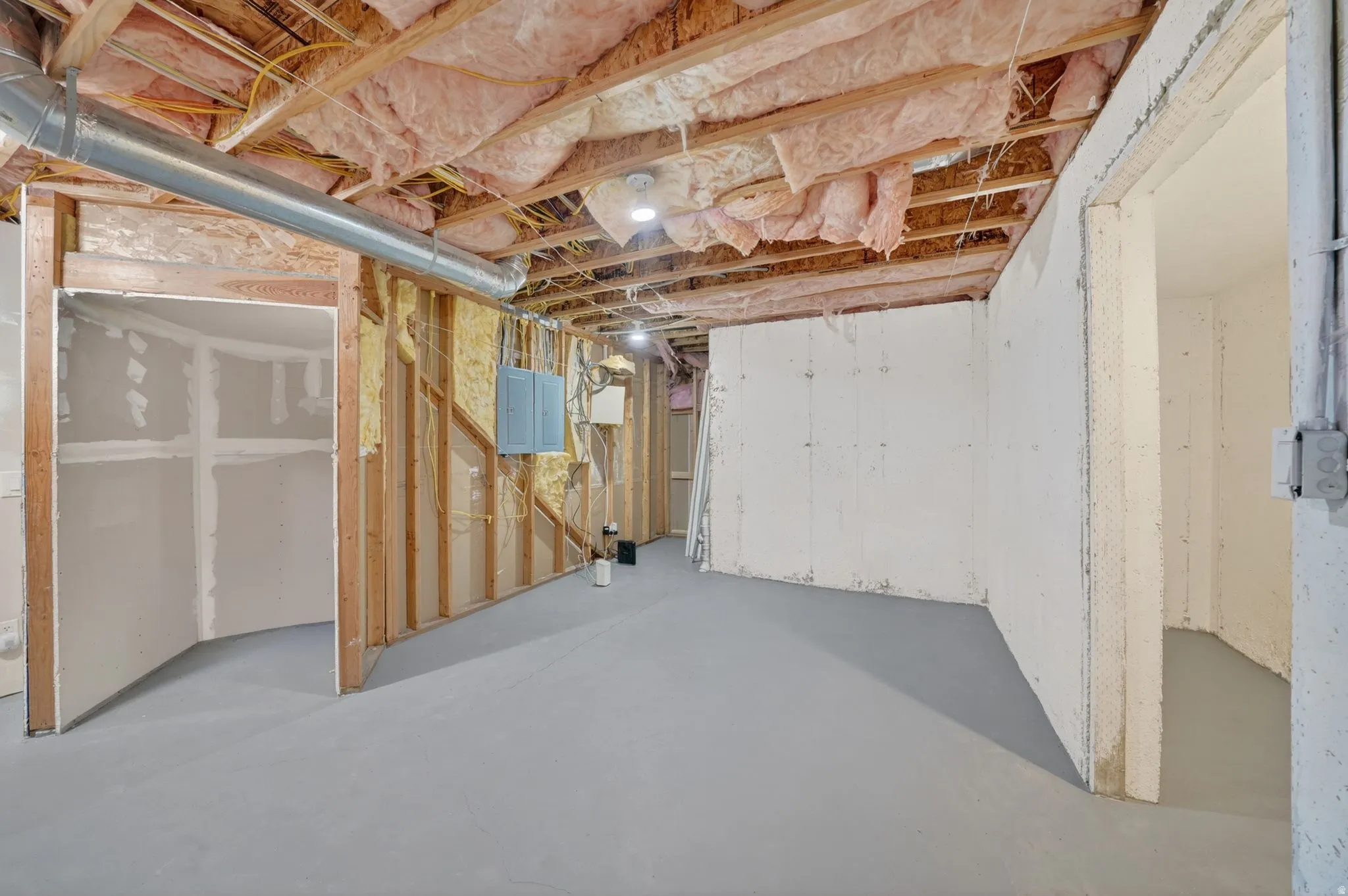 Unfinished basement featuring exposed wood framing, ceiling insulation, concrete flooring, and partial drywall installation