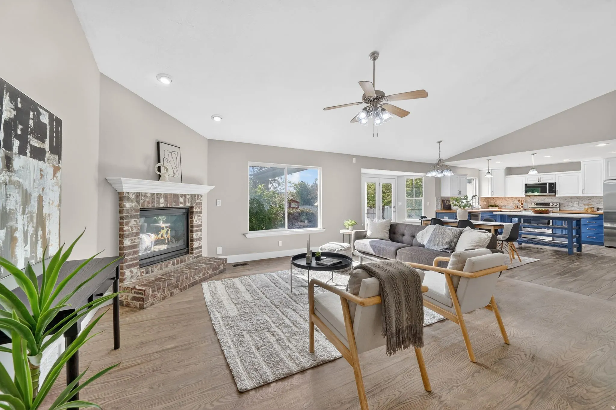 Open-concept living space featuring wood-finish flooring, a brick fireplace with a white mantel, and vaulted ceilings with recessed lighting