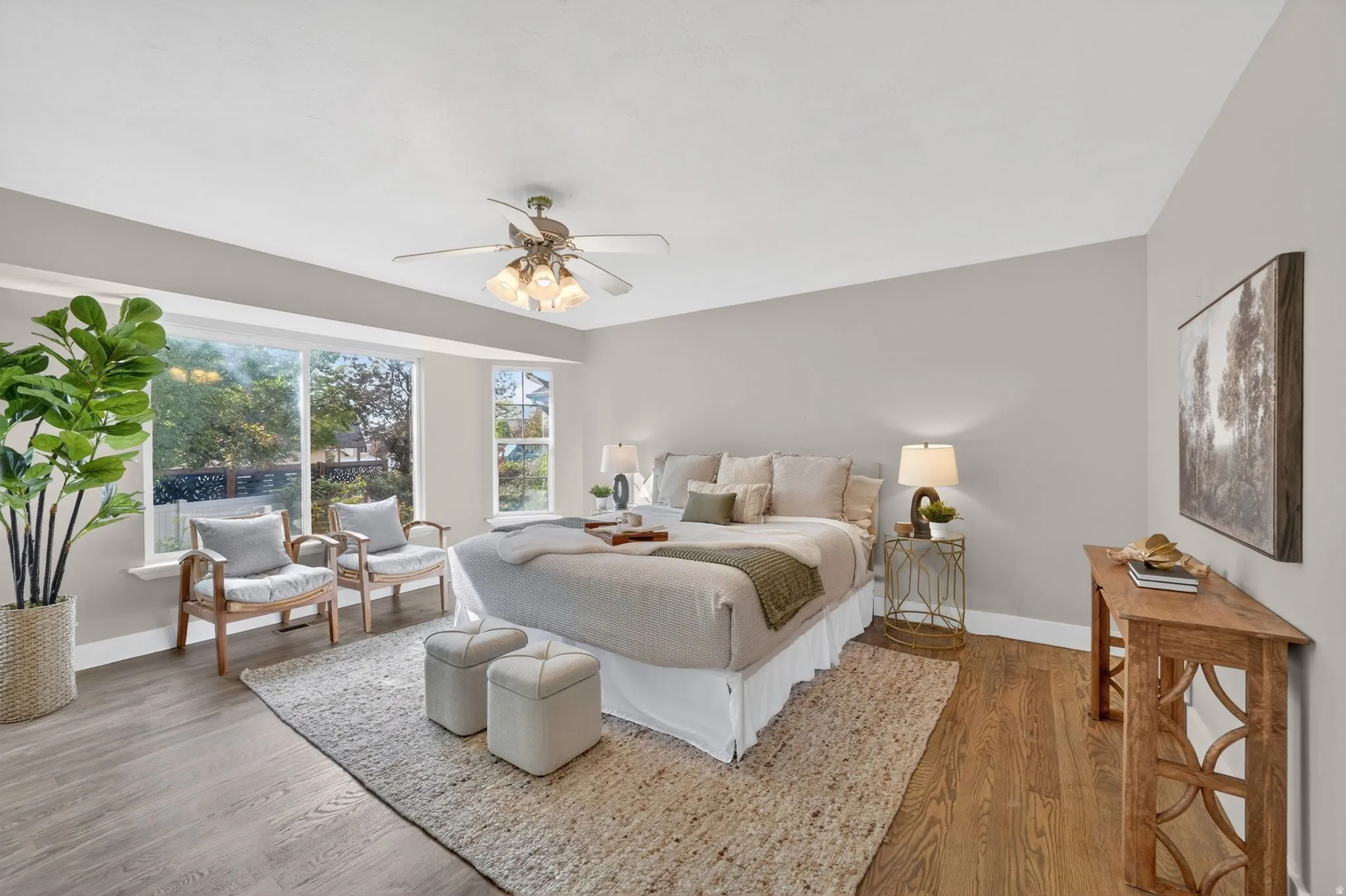 Spacious room featuring a bay window, a ceiling fan with integrated lighting, two distinct wood-finish flooring areas, and a textured area rug