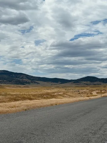 Expansive land parcel featuring a paved road frontage, natural golden grasslands, and distant mountainous terrain