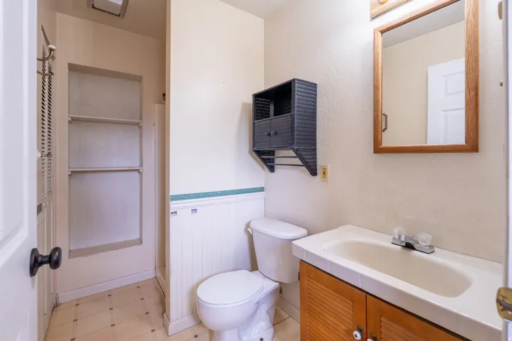 Bathroom featuring a wood-framed mirror, wood-finish vanity with a white countertop and integrated sink, white beadboard wainscoting, and square floor tiles