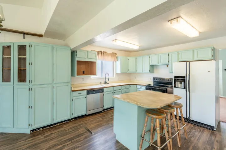 Kitchen featuring abundant cabinetry, a central island with countertop seating, wood-finish flooring, a stainless steel dishwasher, and a double basin sink with a high-arch faucet